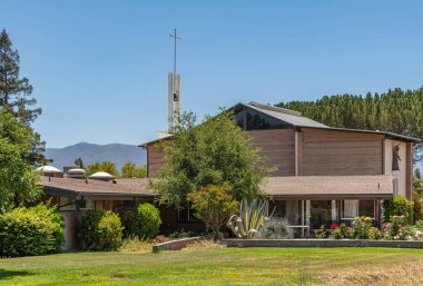 Santa Inez, CA, USA - 3 Nisan 2009 San Lorenzo Semineri. Mavi gökyüzünün altındaki yüksek kilisenin önünde alçak ofis binası olan yeşil yapraklar. Çiçekler renk ekler. 