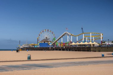 Santa Monica, CA, ABD - 20 Haziran 2013: Feribot Tekerleği, lunapark treni ve iskelede sürekli renkler gösteren daha adil yerler. Önde kumsal var, mavi gökyüzünün altında.. 