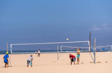 Santa Monica, CA, ABD - 20 Haziran 2013: Arkalarında koyu mavi su ve mavi gökyüzü altında kumlu sahilde voleybol oynayan 4 adam. Giysi renk katar.