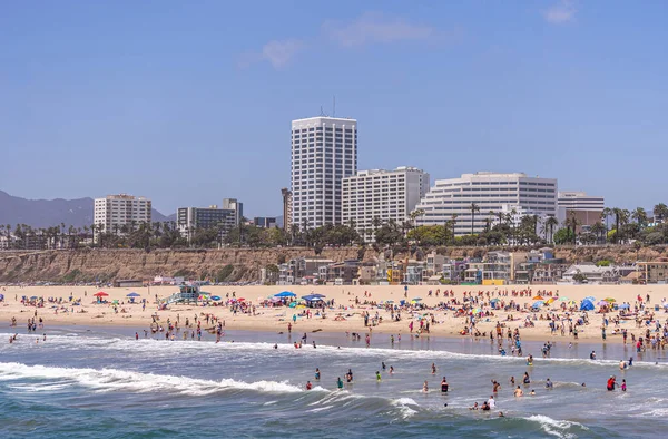 Santa Monica, CA, ABD - 20 Haziran 2013: Plaj ve mavi gökyüzünün hemen kuzeyinde yüzen yüzücülerle dolu. Okyanus Bulvarı 'nda yeşil ağaçları ve kayalık kıyı şeridi olan yüksek binalar..