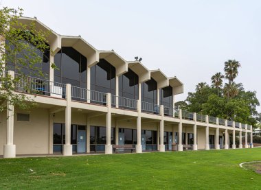 Santa Barbara, CA, USA - 2 Haziran 2021: Şehir kolej tesisleri. Bej rengi taş ve kampüs merkezinin büyük pencereleri yeşil çimlerin arkasında ve gri gökyüzünün altında. Kenarlarında yeşil yapraklar.