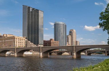 Grand Rapids, MI, USA - June 7, 2008: Grand River with Gillet bridge and Amway Grand Plaza hotel behind under blue sky. 2 tall buildings farther: JW Marriott and Plaza Towers. clipart