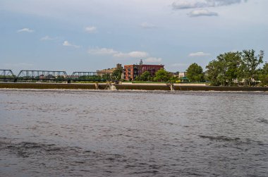 Grand Rapids, MI, ABD - 7 Haziran 2008: Altıncı Cadde Köprüsü 'ndeki yeşil parktaki kırmızı taş bina ve açık mavi bulutların altındaki Newberry Caddesi NW. Nehirde yeşil yapraklar ve gri-kahverengi su.