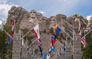 Black Hills, Keystone, SD, USA - 31 Mayıs 2008: Rushmore Dağı. 4 başkanın ünlü heykelinin önünde renkli devlet bayrakları. Mavi bulutların altında gri granit.