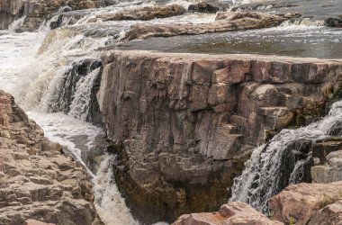 Sioux Falls, SD, USA - June 2, 2008: Closeup of brown-black rock spared from water overflow with splashing white water flows around.