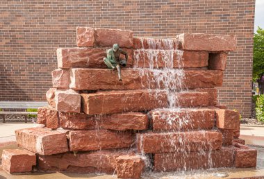 Sioux Falls, SD, USA - June 2, 2008: Closeup of large red stone composition from which white foaming water flows down. Small green bronze statue of man pouring water on top.
