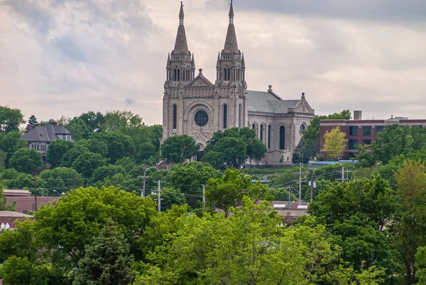 Sioux Falls, SD, USA - June 2, 2008: Beige stone Cathedral of Saint Joseph with 2 towers under white cloudscape and lots of green foliage up front. 