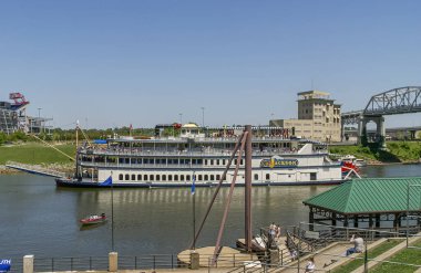 Nashville, TN, ABD - 19 Mayıs 2007: Downtown. Cumberland Nehri 'ndeki beyaz ve kırmızı General Jackson nehir kürekli teknesi kıyı şeridi manzaralı ve mavi gökyüzünün altındaki yaya köprüsü.