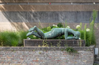 Brugge, Flanders, Belçika - 3 Ağustos 2021: Permeke tarafından Niobe olarak adlandırılan Groenerei boyunca uzanan kahverengi tuğlaların üzerinde uzanan yeşil bronz kadın heykeli. Arkadaki yeşil otlar.