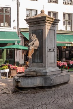Brugge, Flanders, Belçika - 4 Ağustos 2021: At arabası sürücülerinin hayvanlarını sulamak için kullandıkları musluk gibi at başlı su pompası. Wijngaardplein 'de Beguinage' ın yakınına yerleştirilmiş..