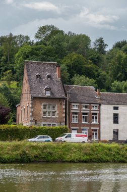 Dinant, Wallonia, Belçika - 8 Ağustos 2021: Soldaki ev İspanyol işgalci tarafından Meuse nehri kıyısında yeşil bir çevrede kurulmuş ve önünde arabaları park edilmiş 16. yüzyıla ait..