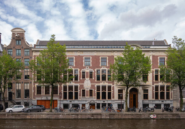 Amsterdam, Netherlands - August 13, 2021: Historic palace turned into multiple dwellings with Roman-Greek sculptures and frescos on Herengracht 531-537. Bikes and green foliage.