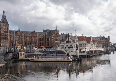 Amsterdam, Hollanda - 14 Ağustos 2021: Red Stone Merkez Tren İstasyonu 'nun doğu yakası, ağır bulutlar altında, tekne, restoran ve panton su üzerinde ziyaretçi merkezi.