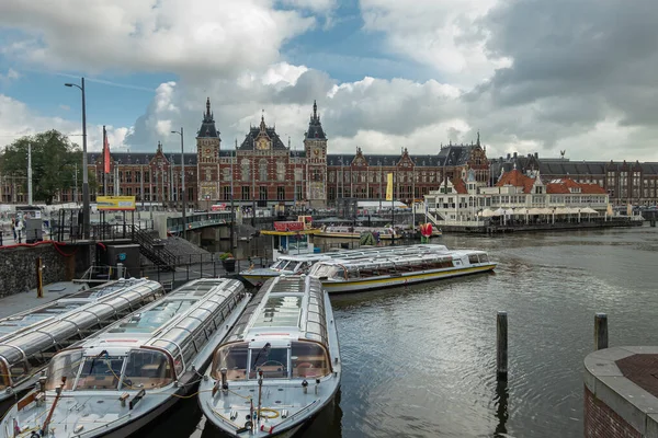 アムステルダム オランダ 8月14 2021 青の雲の下で赤と金の中央鉄道駅の前にドッキング観光運河ボートのグループ 旅行者との忙しいシーン — ストック写真