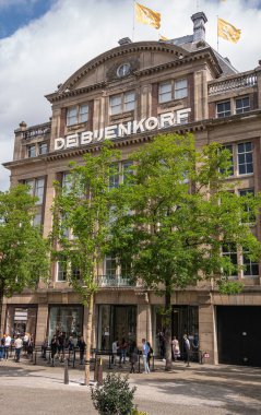 Amsterdam, Hollanda - 14 Ağustos 2021: Barajdaki ünlü lüks mağaza De Bijenkorf 'un ön cephesi ve ana girişi. Covid-19 müşterileri dışarıda sırada beklemeye zorluyor..