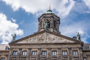 Amsterdam, Hollanda - 14 Ağustos 2021: Mavi bulutlar altında Royal Palace 'ın ön kahverengi taş anıtsal gable ve saat kulesinin kapatılması. Yoğun fresk ve bronz heykeller.