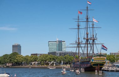 Amsterdam, Hollanda - 15 Ağustos 2021: Tarihi otantik 3 direkli tüccar gemisi Barquentine-model adını mavi gökyüzü altında almıştır. Yüksek binalarla daha geniş manzara.