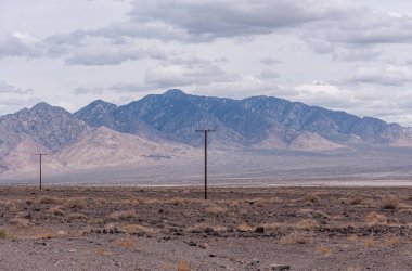 High Desert, Nevada, ABD - 17 Mayıs 2011: Gri bulutlar altında kahverengi elektrik direkleriyle kahverengi çalıların üzerinde geniş bir manzara. Arkaplan olarak karanlık dağ aralığı.