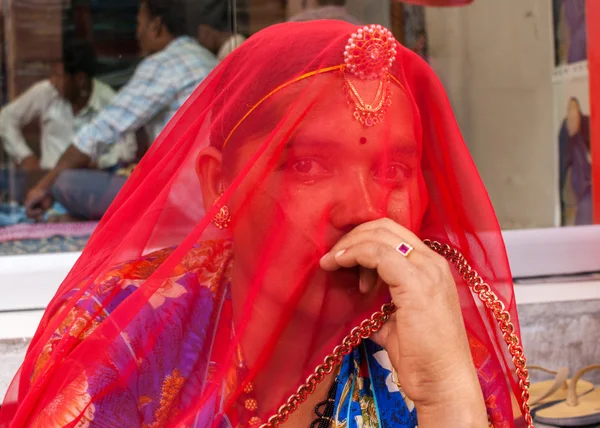 Kadın yüzünü kırmızı örtü ile gizler.