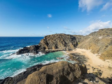 Honolulu, Oahu, Hawaii - 12 Temmuz 2025: Pasifik Okyanusu 'ndaki Halona sahili. Kayalara ve kuma çarpan sörfler, mavi bulutların altındaki otoban