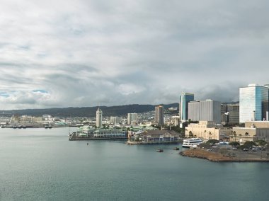 Honolulu, Oahu, Hawaii - July 12, 2025: Cityscape. The harbor, Aloha Tower on Pier 9 with green retail buildings and high-rise residential towers on the right under gray cloudscape