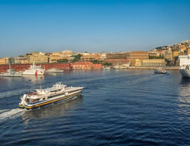 Napoli, İtalya - 17 Temmuz 2024: Liman manzarası. NLG feribot. Sahil Güvenlik gemileri ve şehir manzarası arkada. Palermo Rıhtımı ve kırmızı binaları ile Enrico Caruso Müzesi ve Parthenope Üniversitesi sağda.