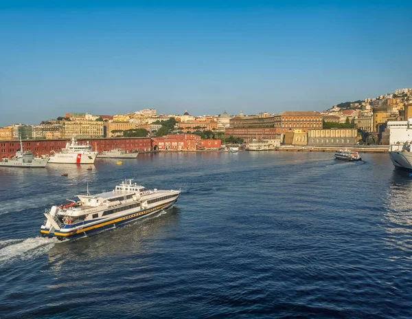 Napoli, İtalya - 17 Temmuz 2024: Liman manzarası. NLG feribot. Sahil Güvenlik gemileri ve şehir manzarası arkada. Palermo Rıhtımı ve kırmızı binaları ile Enrico Caruso Müzesi ve Parthenope Üniversitesi sağda.