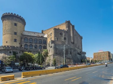 Napoli, İtalya - 17 Temmuz 2024: Tarihi Castel Nuovo köşe kulesi, surlar ve limanın hemen dışındaki işlek otoyol boyunca bina. Araba ve motosiklet trafiği