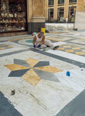 Napoli, İtalya - 17 Temmuz 2024: Galleria Umberto 1, camdan kanatlı alışveriş merkezi. Kadın işçi mermer mozaik zemini temizliyor