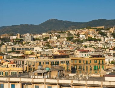 Messina, Sicily, Italy - July 18, 2024: urban jungle or cityscape scenery from downtown with green mountain range in back. under blue sky as seen from harbor