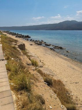Messina, Sicilya, İtalya - 18 Temmuz 2024: Sicilya ve İtalya arasındaki boğazdır. Sahilde kuzeye bakıyor. Kayalık sahil koruma hatları var. Mavi bulutlar altında anakara sıradağları