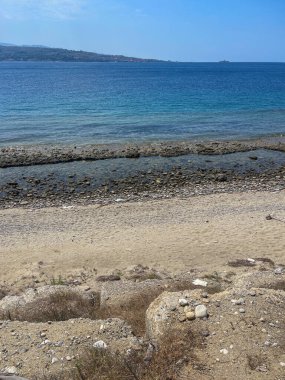 Messina, Sicilya, İtalya - 18 Temmuz 2024: Sicilya ve İtalya arasındaki boğazdır. Çakıl taşlı sahil boyunca güneye bakıyor. Mavi bulutlar altında anakara sıradağları