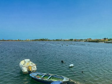 Messina, Sicilya, İtalya - 18 Temmuz 2024: Pisciculture: Pantano Piccolo gölündeki balık çiftliği yarımadanın en batı noktasında. Ön tarafta küçük bir tekne var.