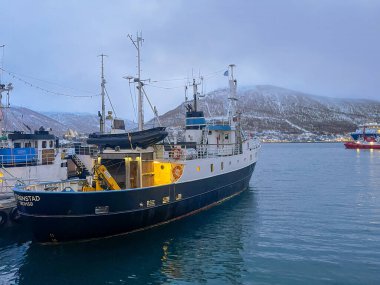 Tromso, Norveç - 23 Aralık 2025 Stronstad balıkçı teknesi limana yanaştı. Anakara dağı ve şehir manzarası arkada.