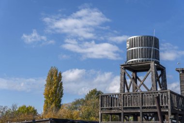 Büyük ahşap bir su kulesi renkli sonbahar ağaçlarıyla çevrili ahşap bir platformda oturur. Pofuduk bulutlu parlak mavi gökyüzü güneşli bir günde çarpıcı bir zemin oluşturur..