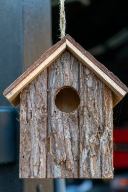 Doğal ahşaptan yapılmış el yapımı bir kuş evi kancaya asılır. Dokulu yüzeyi çevreyle harmanlanır ve kuşlar için rahat bir yuva sağlar..