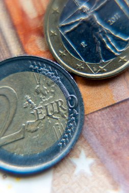 Bir banknotun üzerine iki avro para yerleştiriliyor. Bozukluklar farklı tasarım ve özellikleri gösteriyor. Olay yeri para birimini ayrıntılı olarak yakalıyor. Arkaplan nottaki renkleri içeriyor.