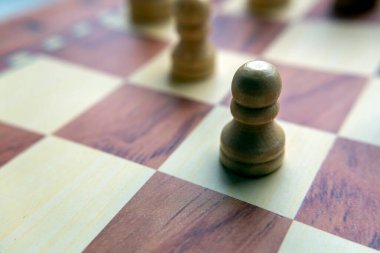 Satranç tahtasına yerleştirilmiş tahta bir satranç taşının yakın plan görüntüsü. Satranç taşı ön planda, tasarımının detaylarını gösteriyor. Arkaplan bulanık.