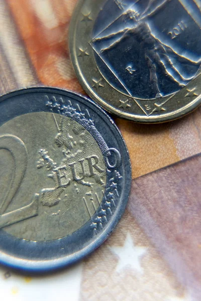 Bir banknotun üzerine iki avro para yerleştiriliyor. Bozukluklar farklı tasarım ve özellikleri gösteriyor. Olay yeri para birimini ayrıntılı olarak yakalıyor. Arkaplan nottaki renkleri içeriyor.