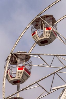 Bir lunaparktaki bulutlu gökyüzünde dönme dolabın manzarası görülebilir. Yapı, metal iskelet ve ışıklarla yüksek duruyor. Ziyaretçiler yukarıda gezmekten hoşlanırlar..