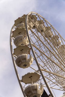 Mavi gökyüzüne karşı bir dönme dolap dik durur. Yolcu kabinleri yavaş hareket ederek, sürücülerin şehir manzarasının keyfini çıkarmalarına olanak sağlıyor. Ortalık insanlarla dolu..