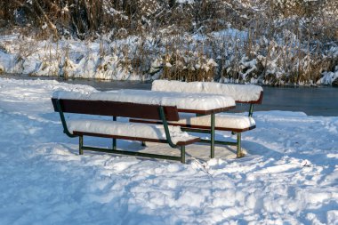 Nehrin kenarında karla kaplı iki bank var. Çevrede beyaz kar ve çıplak ağaçlar var. Sahne, insanların olmadığı bir kış gününü yakalıyor..
