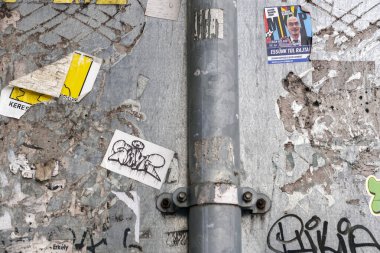 Şehirdeki bir duvar farklı çıkartmalar ve posterlerle kaplıdır. Bazı tasarımlar renklidir, diğerleri basit ve monokromatiktir. İnsanlar her gün bu duvarın önünden geçebilir..