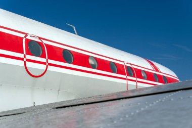 Bir JAK-40E uçağı parlak bir ayarda duruyor. Yan taraftaki kırmızı detaylar göze çarpıyor. Gökyüzü açık. Uçak pencerelerini ve yapısını cesurca gösteriyor..