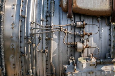 Jet motorunun metal parçaları tezgahta görülebilir. Motor kaplaması boyunca çeşitli borular ve bağlantılar düzenlendi. Aletler ve ekipmanlar parlak ışık altında bölgeyi çevreledi..