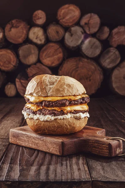 Double burger with cheddar cheese and firewood pile in background