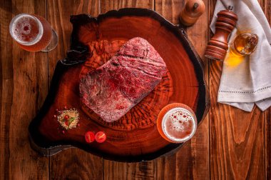 Tahta kesme tahtasının üzerinde iki bardak birayla ızgara Denver bifteği. Mermer et - Üst Manzara.