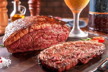 Dilimlenmiş ızgara biftek ve tahta kesme tahtasının üzerinde iki bardak bira. Mermer et (Brezilya picanha 'sı).
