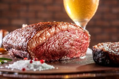 Tahta kesme tahtasının üzerinde ızgara kesilmiş biftek ve bir bardak bira (Brezilya picanha).