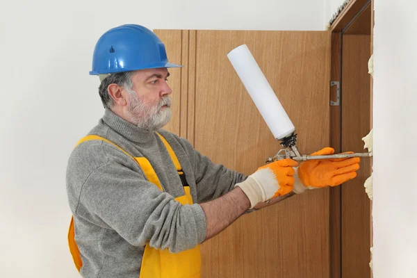 Worker installing wooden door, using polyurethane foam — Stock Photo, Image